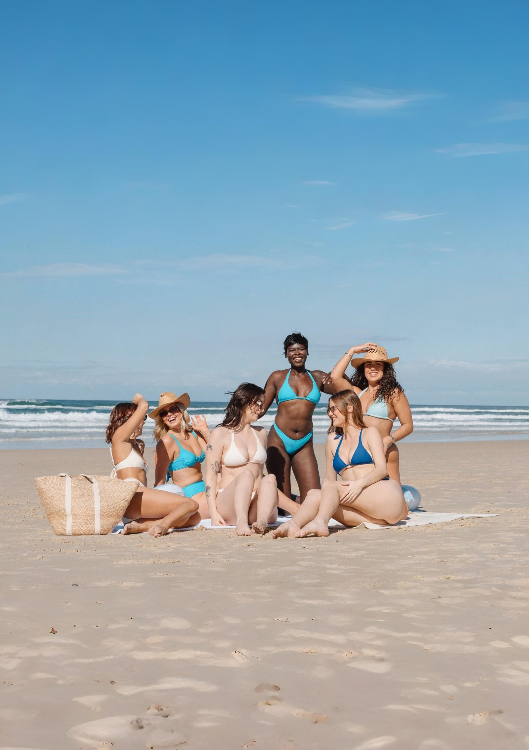 Blue Apparel women in sustainable bikinis sitting on a beach towel under clear blue sky
