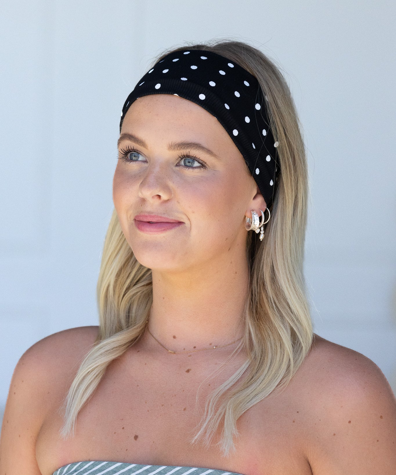 Woman wearing a black polka dot headband against a light gray background