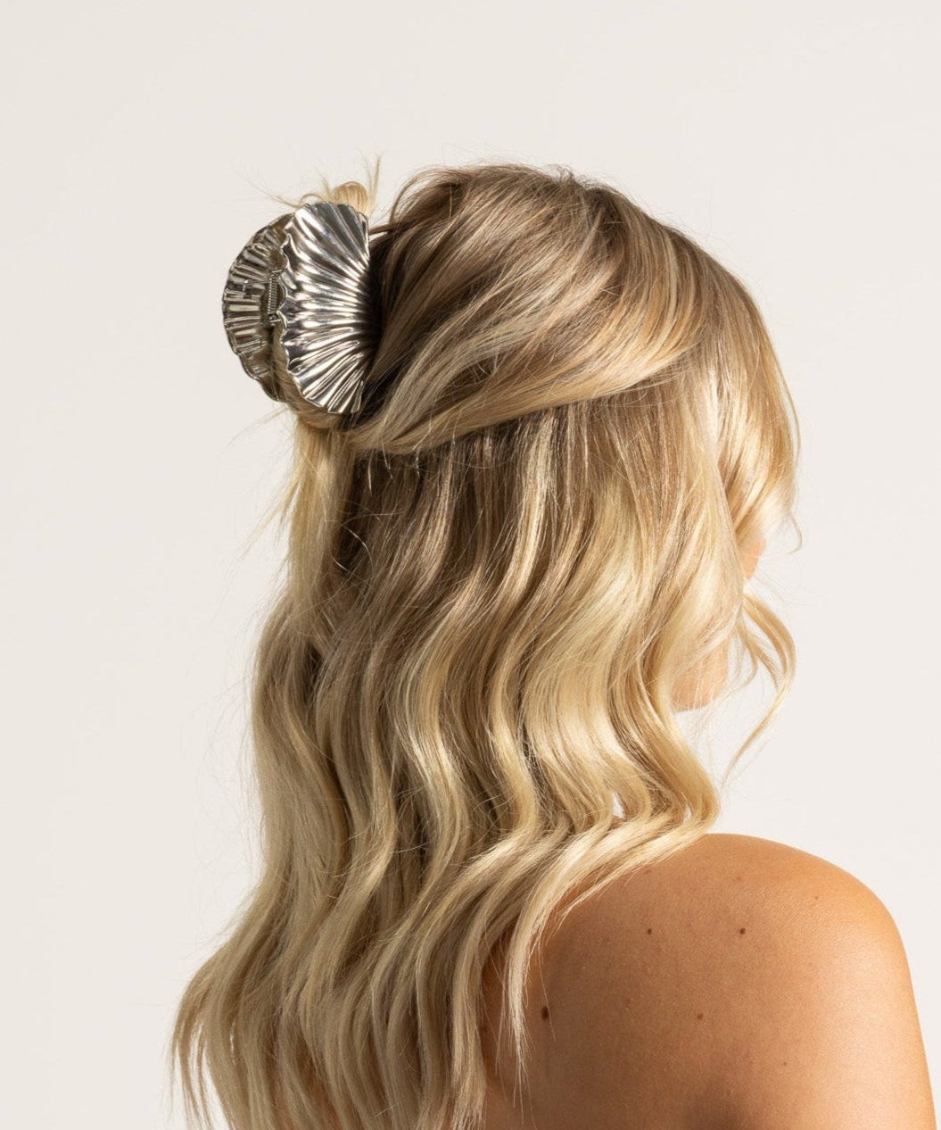 Blonde woman with hair in a bun, decorated with a shell, wearing a light blue top.