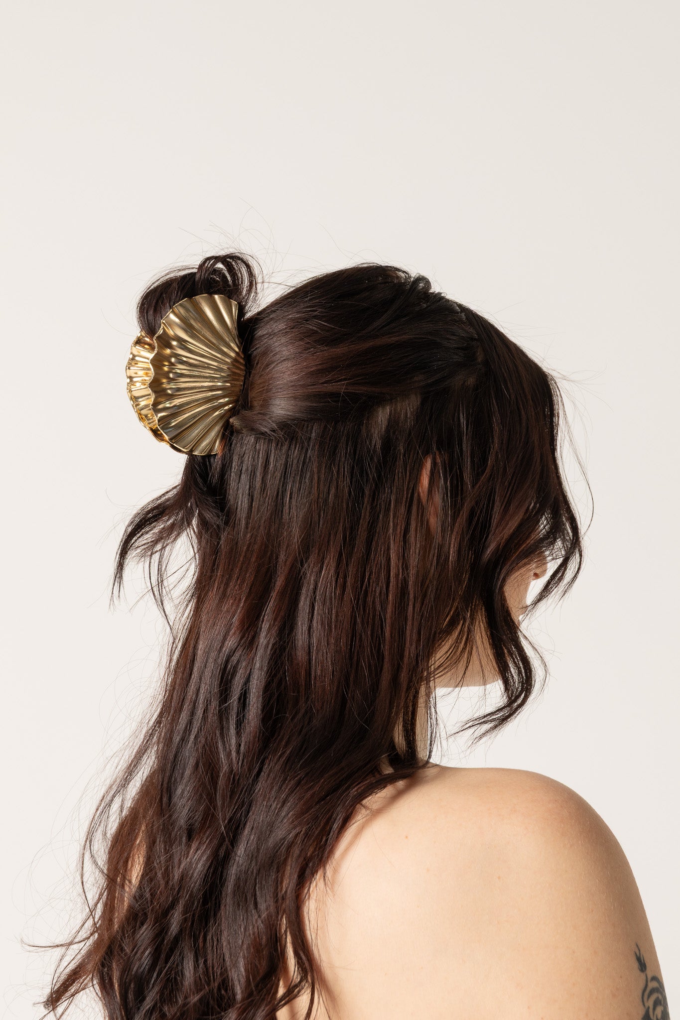 Woman with black hair in a bun, decorated with a shell, wearing a light blue top.