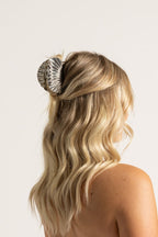 Blonde woman with hair in a bun, decorated with a shell, wearing a light blue top.